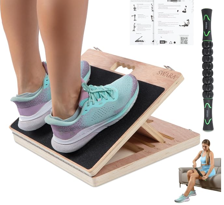 Feet in sneakers standing on the Swara 14-inch foldable wooden slant board, shown with the included quick-start guide and Swara muscle roller